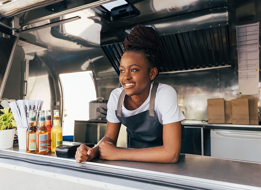 Food Truck Insurance - Smiling Woman in an Apron Leaning Over the Counter and Working in a Food Truck